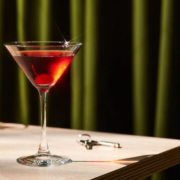 Manhattan cocktail on a wooden table with a green background