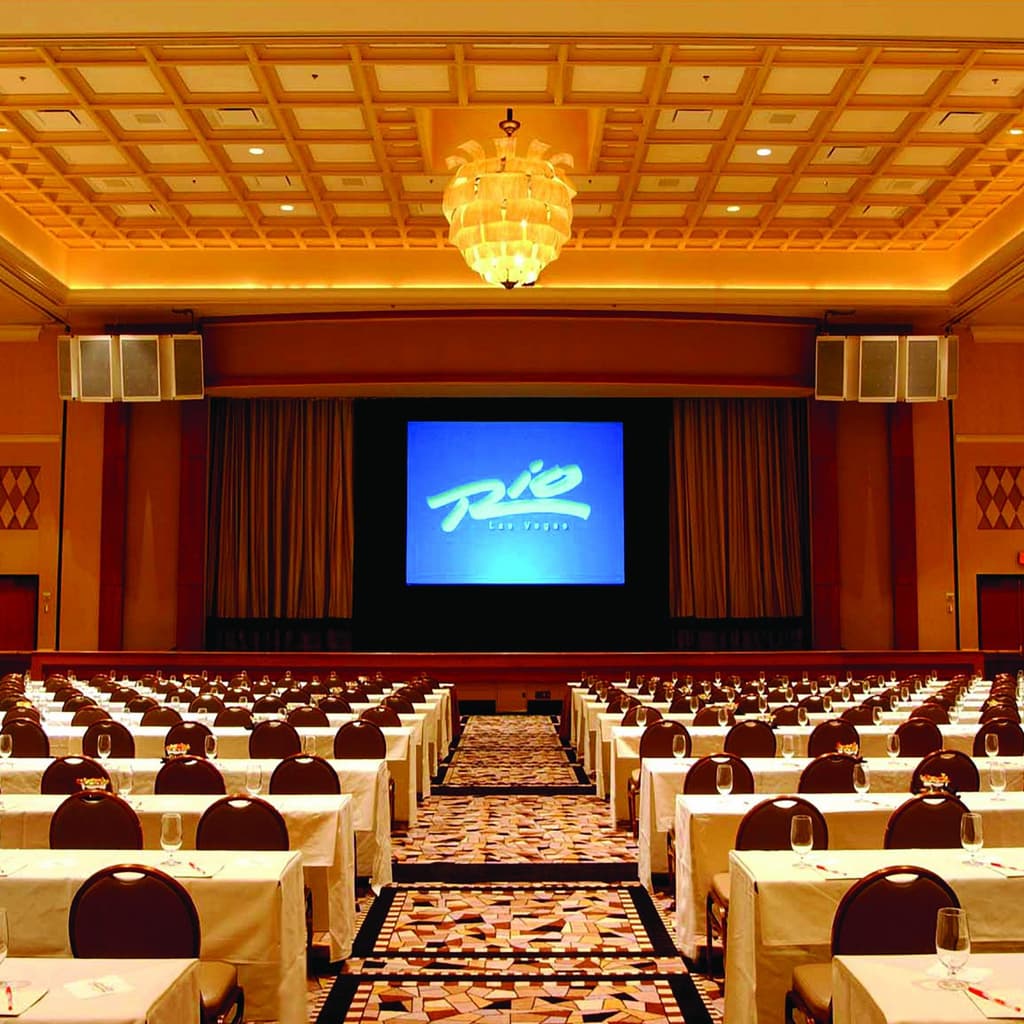 Brasilia Ballroom Image with stage and large screen along with rows of tables for attendees at a conference at Rio Hotel & Casino Las Vegas