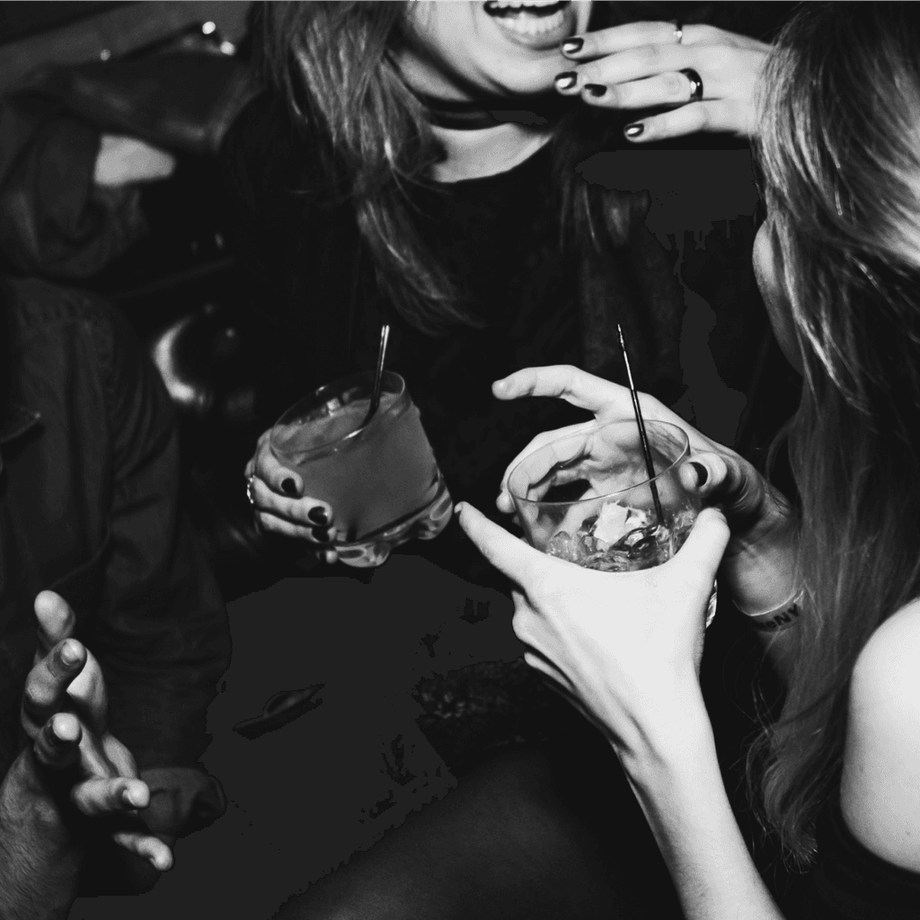 Women laughing and holding cocktails in dim restaurant